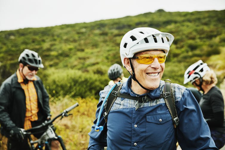 smiling man in bike helmet in foreground of a bike group pit stop
