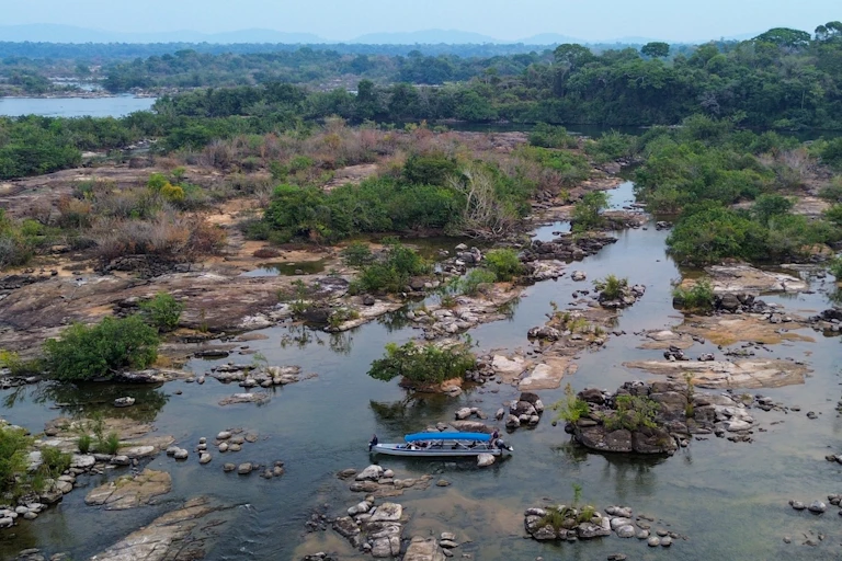 Imagem mostra um barco em meio a um trecho de rio com água baixa e bancos de areia e rocha