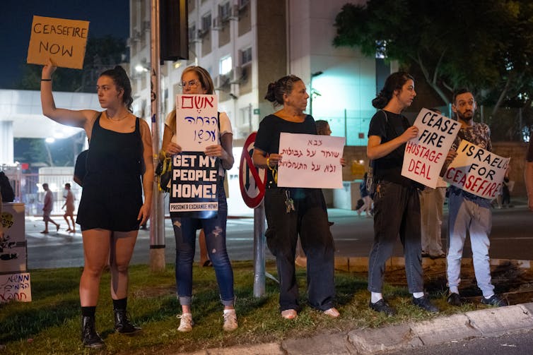 Un groupe de femmes manifestant la nuit et portant des pancartes indiquant des choses comme « Cessez le feu, accord sur les otages ».