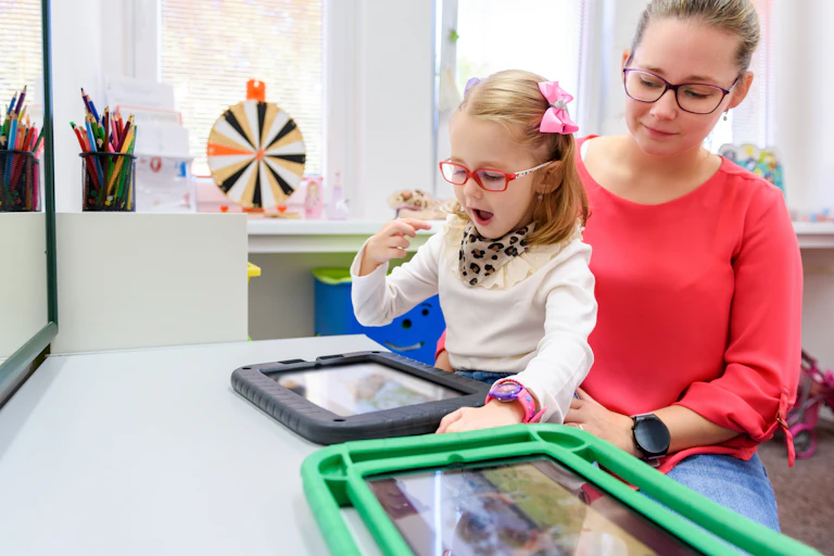 A young girl sitting on a woman's lap uses a tablet device.