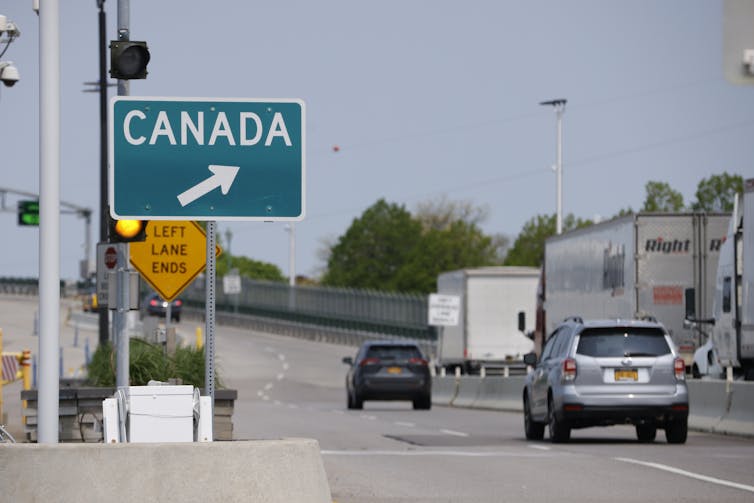 Cars drive passed a highway sign directing traffic toward Canada.