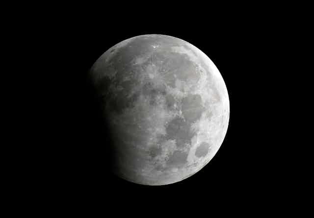 The moon, partially shadowed on the left side, against a black background. 