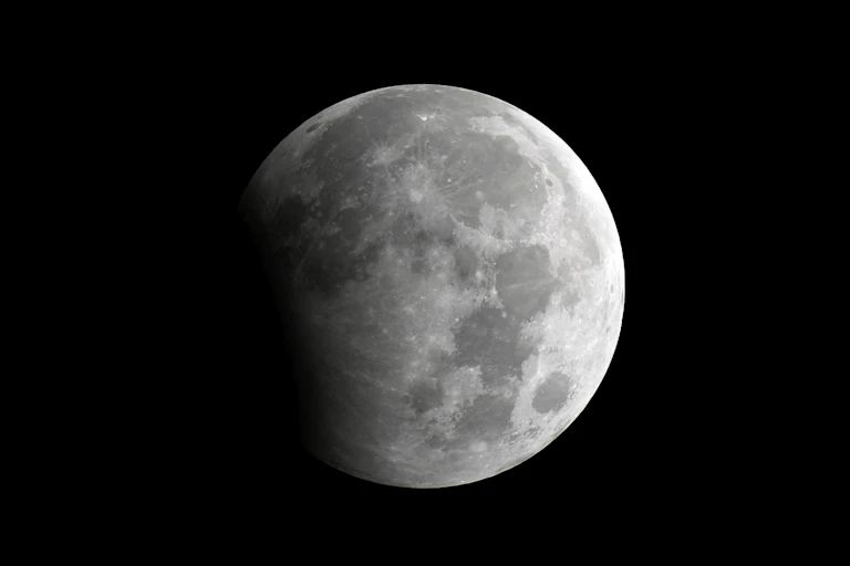 The moon, partially shadowed on the left side, against a black background.