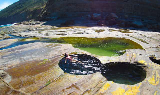A rocky outcrop with a small natural pool of two joined circles and a woman floating in it