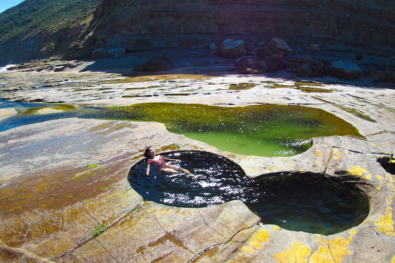 A rocky outcrop with a small natural pool of two joined circles and a woman floating in it