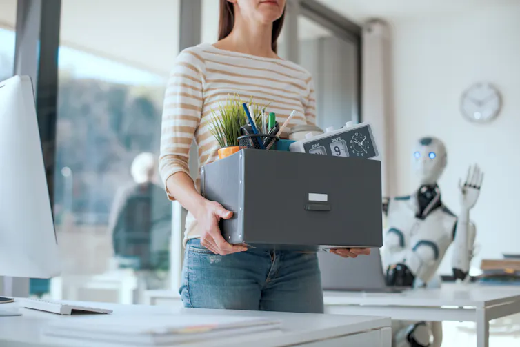 Woman carrying box of her belongings out of an office as robot waves her goodbye