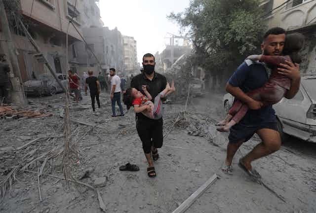 Men carry wounded children away from debris in a warzone