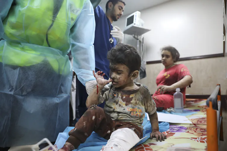 An injured young boy sits next to a healthcare worker