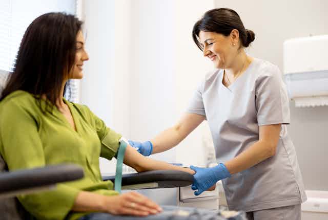 woman sits as nurse performs blood draw on arm