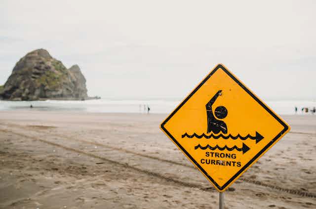 yellow sign showing warning about currents at the beach
