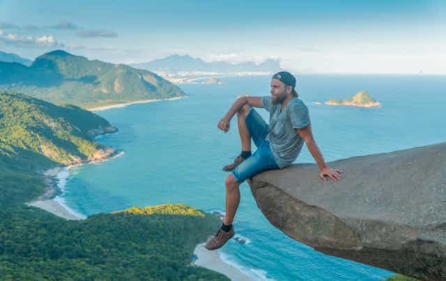 man sitting on risky rock high above sea