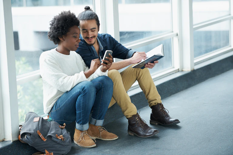 A college couple sitting closely together looking mobile phone screen