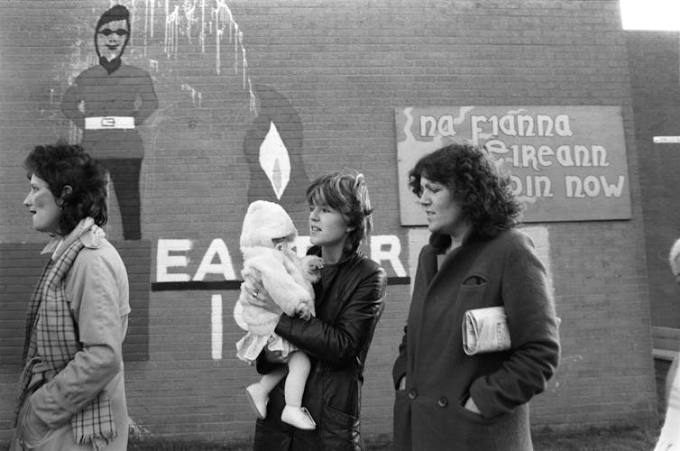 A black and white archival photograph of women and children in front of a wall.