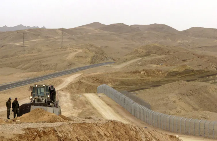 A large expanse of desert is seen with a bulldozer and soldiers in the foreground.