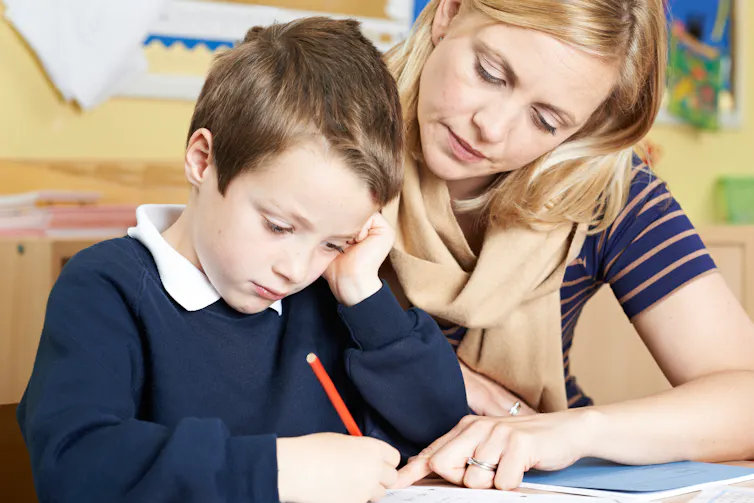 Little boy at school writing with teacher helping
