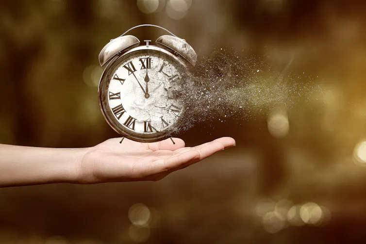 Old-style alarm clock hovers over outreached hand, slowly disintegrating