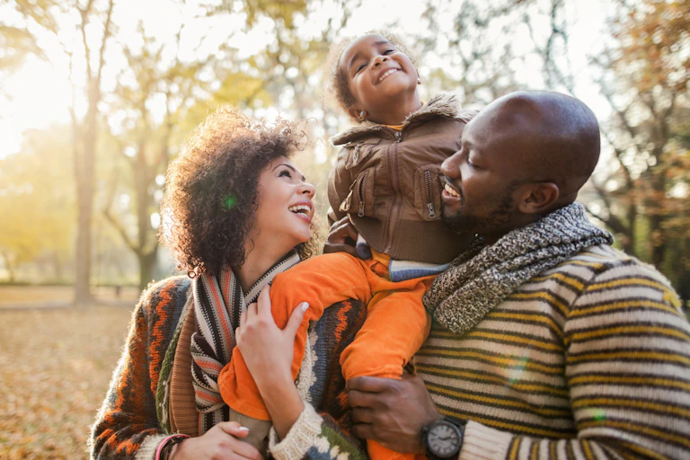 man and woman hold smiling girl on their shoulders