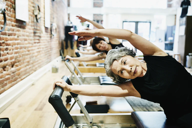 Mujeres maduras haciendo ejercicios en equipos de pilates en un gimnasio.