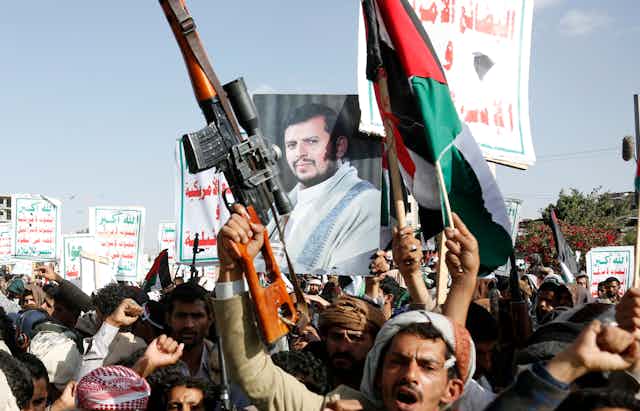 A man holding aloft a rifle is seen in front of other protesters holding an image of a bearded man.