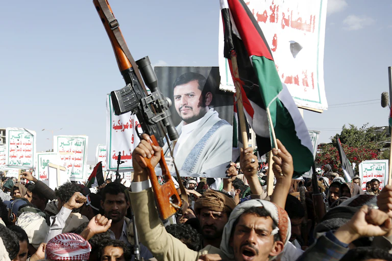 A man holding aloft a rifle is seen in front of other protesters holding an image of a bearded man.