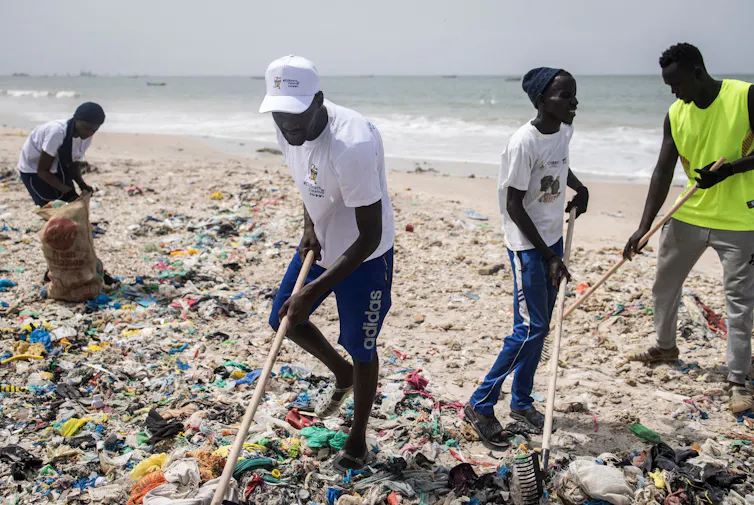 People rake up garbage on a sandy beach.