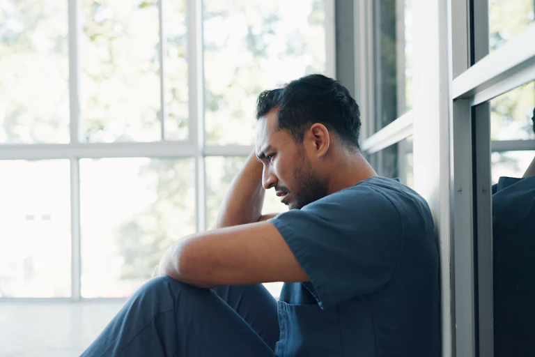 A male health-care workers sitting on the floor, appears stressed.