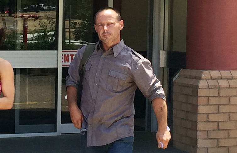 A man in a grey shirt walks in front of a courthouse.