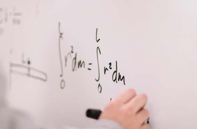 A hand writes an equation on a whiteboard.