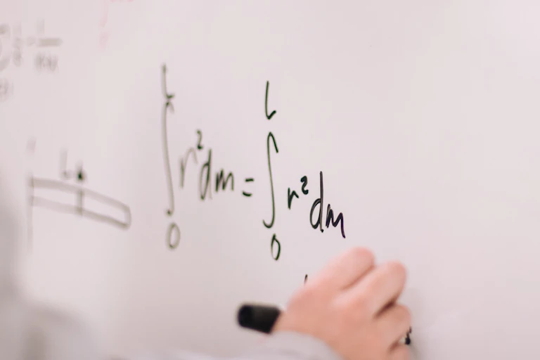 A hand writes an equation on a whiteboard.