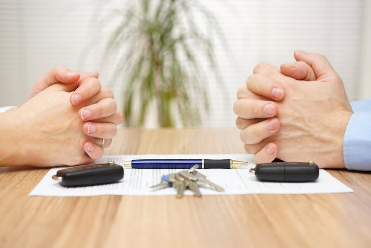 Close up of man and woman's hands resting on paperwork, car keys and house keys