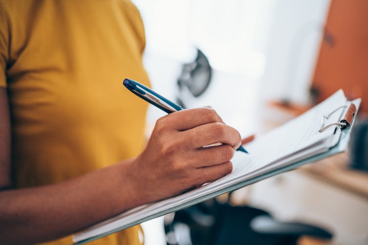 Person writing on a piece of paper on a clipboard with a pen