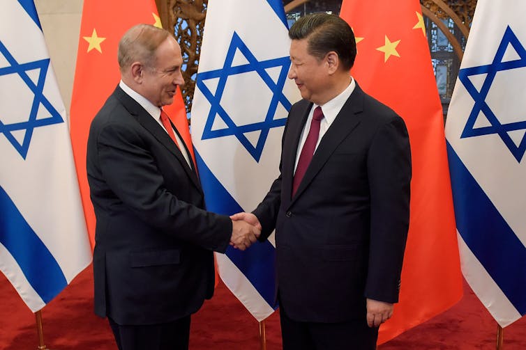 Two men in suits shake hands in front of Chinese and Israeli flags.