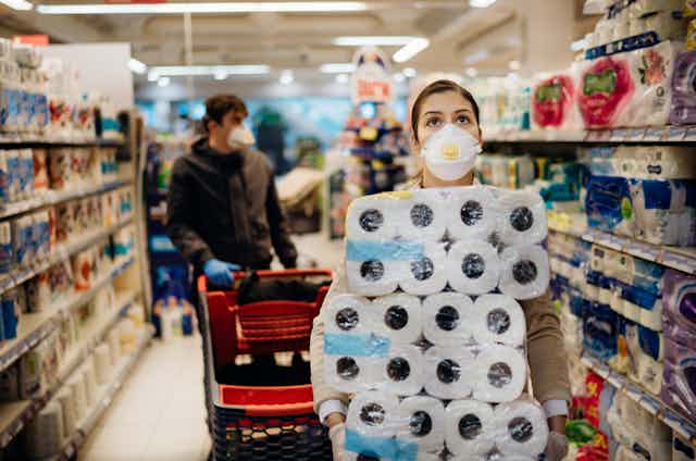 A woman in a face mask holding an armful of toilet paper in a store aisle