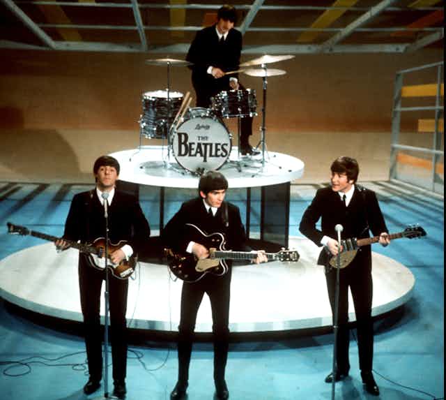 The Beatles on stage in the 60s in black suits