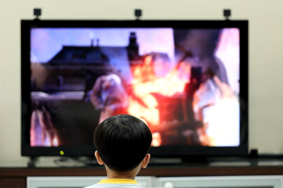 Un enfant de dos est en train de regarder des images floues à la télévision.