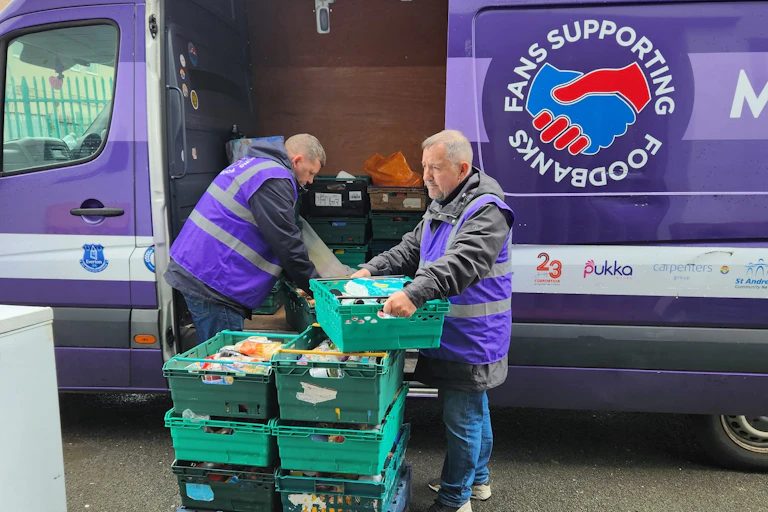 Two men loading crates of food into a fan.
