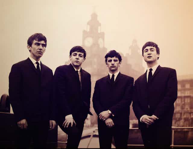 A black and white image of the Beatles in the early 1960s dressed in black suits.