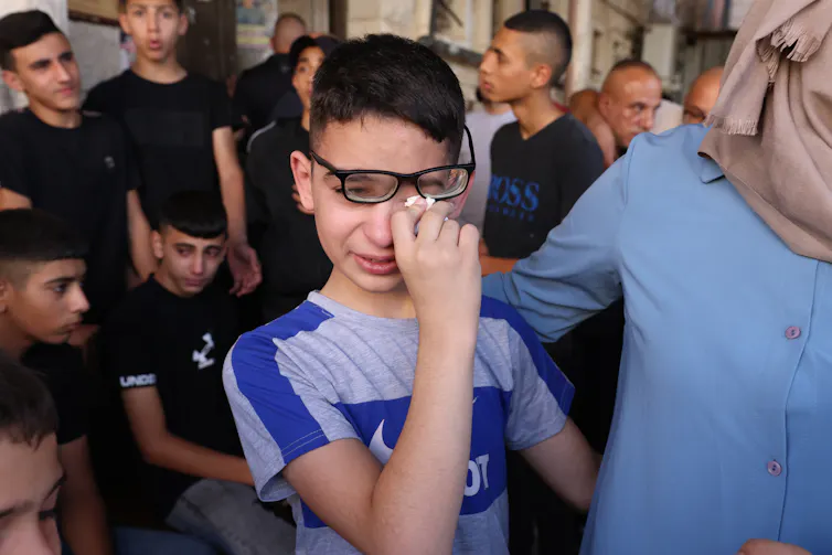 A young Palestinian boy wipes his eye as he cries over the death of a friend.