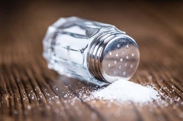 Salt shaker spilling salt on a wooden surface