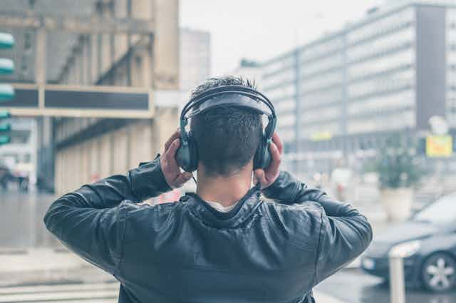 Un hombre de espaldas sujetando unos auriculares mientras escucha música.