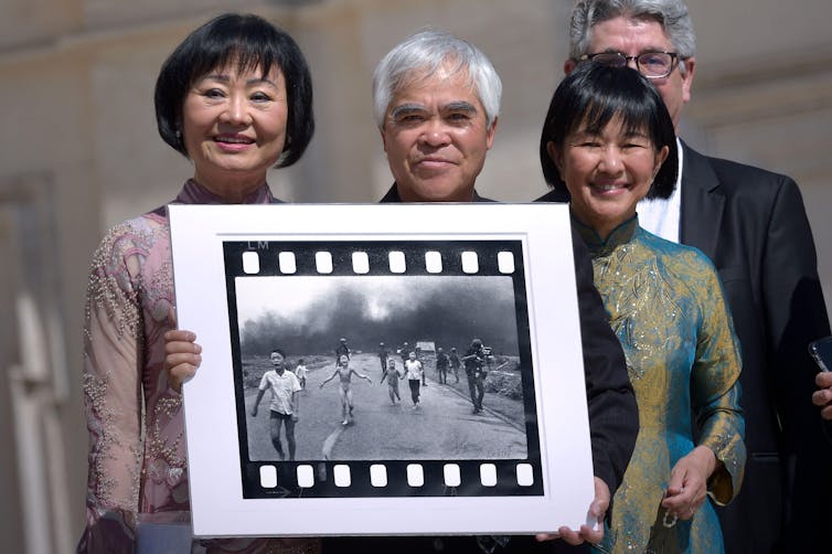 Four people next to a photograph known as 'Napalm Girl' taken during the Vietnam War