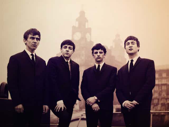 Uma imagem em preto e branco dos Beatles no início da década de 1960, vestidos com ternos pretos.
