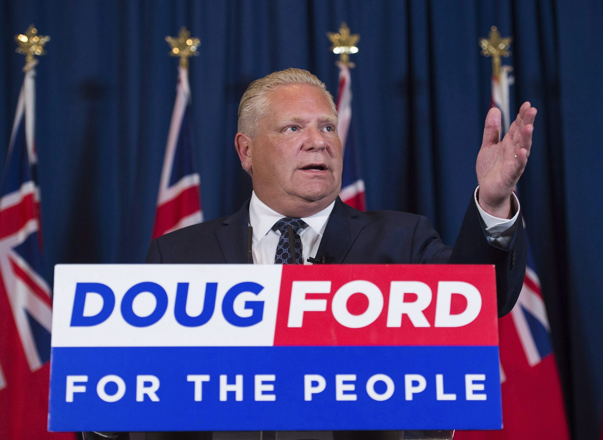 A man seen in a suit with a sign that says Doug Ford for the People.