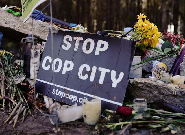 A small sign that reads 'Stop cop city' rests on a pile of stones and flowers.