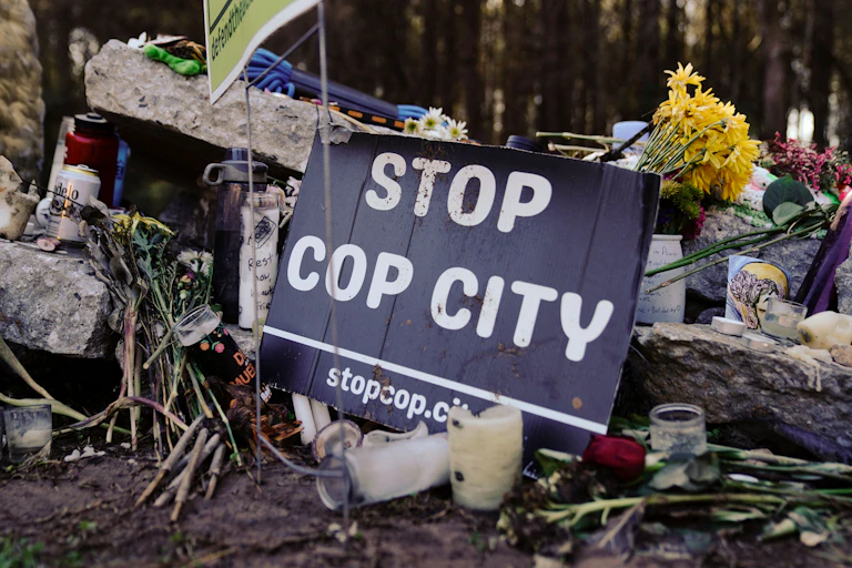 A small sign that reads 'Stop cop city' rests on a pile of stones and flowers.