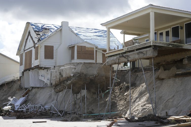 Homes hang over the edge of a cliff above an ocean beach.