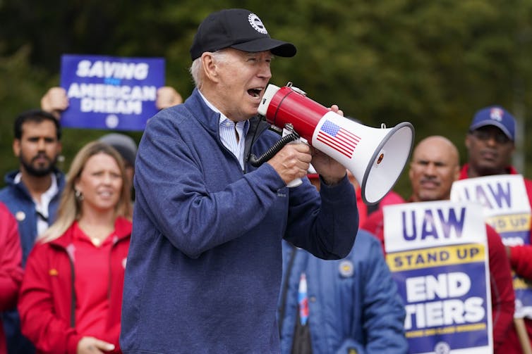 An older man in a ball cap speaks into a megaphone on a picket line.