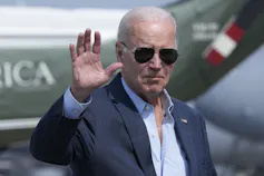 An older man in sunglasses waves.