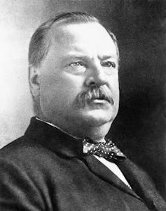 A black-and-white photo of a round-faced man with a moustache.