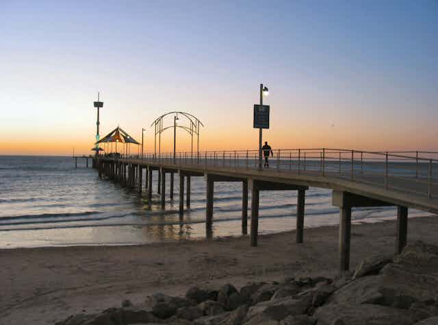 A man walking down a jetty at sunset.